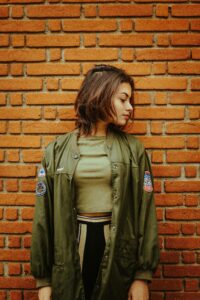 Young woman in stylish jacket poses by a brick wall, showcasing urban fashion.